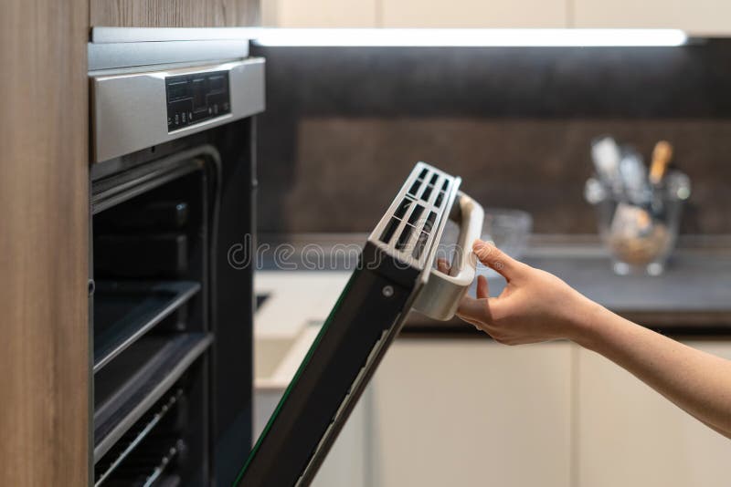 Woman hand opening door of built-in oven in kitchen cabinet