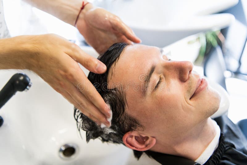 Profile view of a young man getting his hair washed and his head massaged in a hair salon. stock photo Profile view of a young man getting his hair washed and his head massaged in a hair salon. stock photo