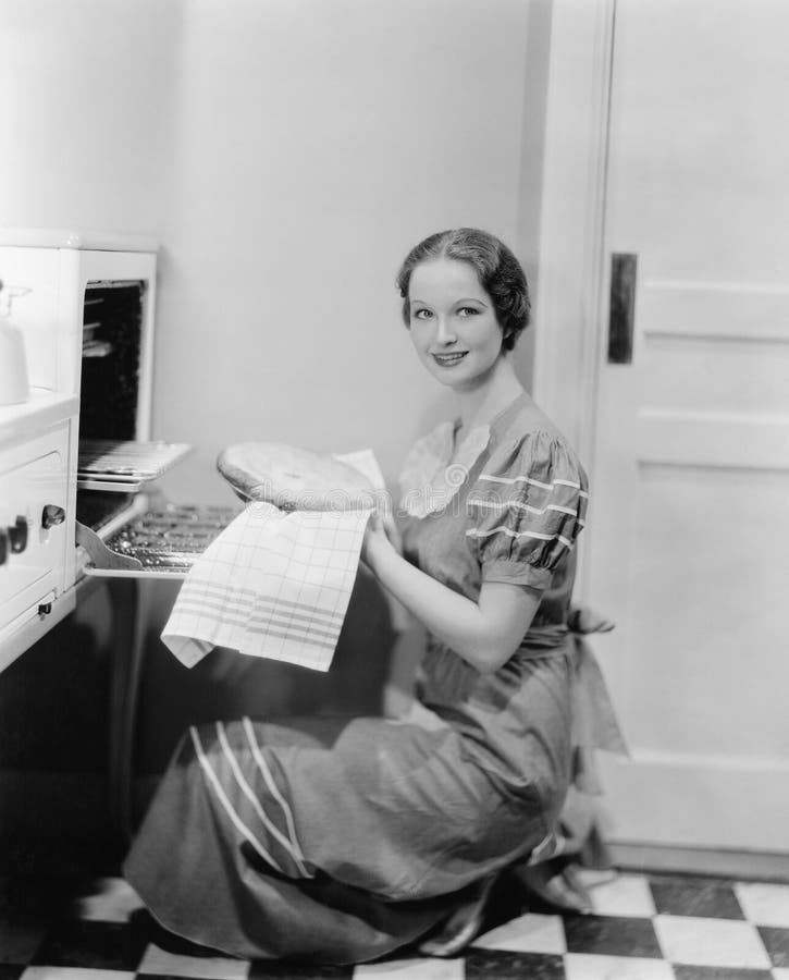 Profile of a young woman taking a pie out of the oven, smiling at the camera