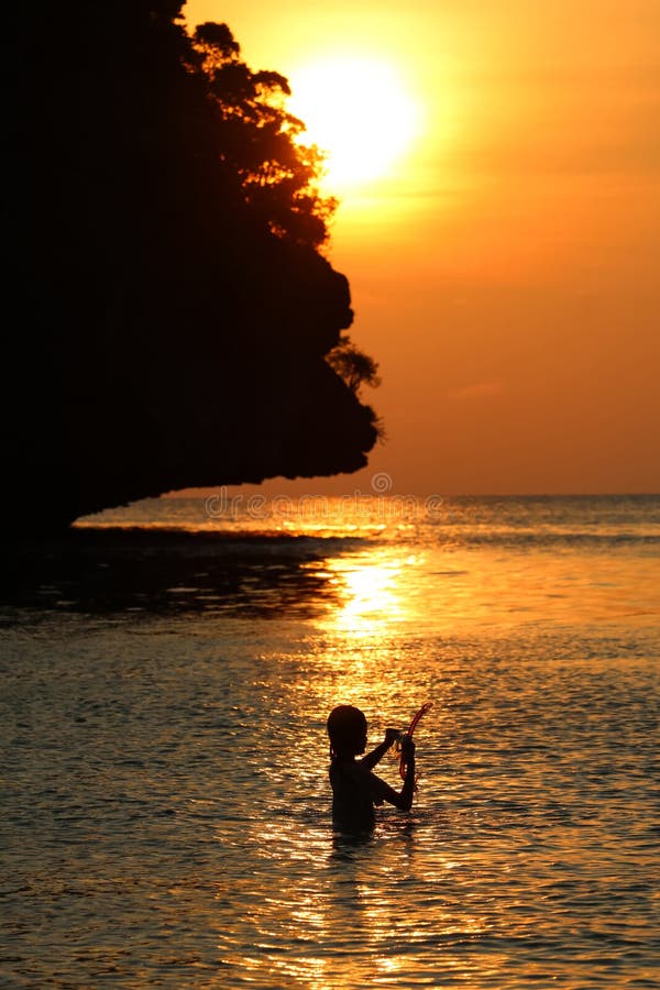 Profili la bambina per godere di di nuotare e immergersi vicino alla spiaggia con il cielo rosso ed il tramonto immagini stock libere da diritti Profili la bambina per godere di di nuotare e immergersi vicino alla spiaggia con il cielo rosso ed il tramonto immagini stock libere da diritti
