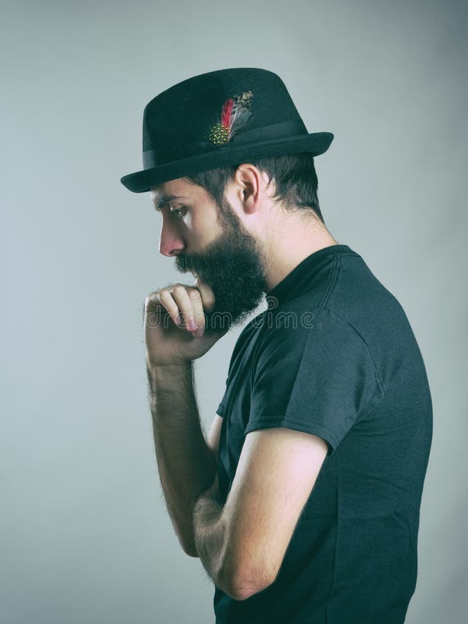 Profilo di vista laterale dei pantaloni a vita bassa seri barbuti che pensano e che guardano giù fotografia stock Profilo di vista laterale dei pantaloni a vita bassa seri barbuti che pensano e che guardano giù fotografia stock