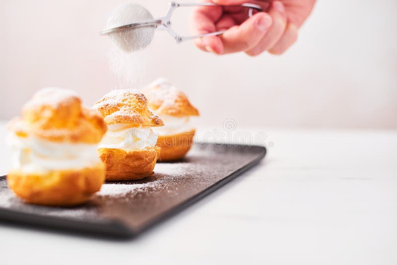 Profiteroles délicieuses avec de la crème et le sucre en poudre d'un plat images stock Profiteroles délicieuses avec de la crème et le sucre en poudre d'un plat images stock