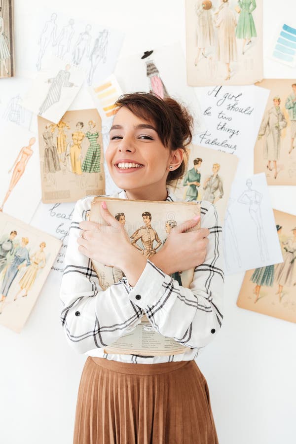 Progettista adorabile di fahion della giovane donna che tiene il suo sketchbook immagine stock Progettista adorabile di fahion della giovane donna che tiene il suo sketchbook immagine stock