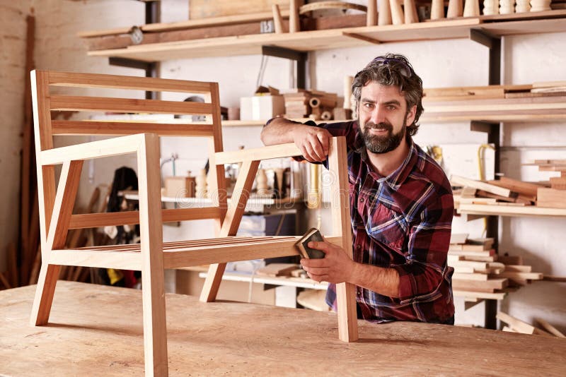 Progettista della mobilia dell'artigiano che insabbia una sedia nella sua officina