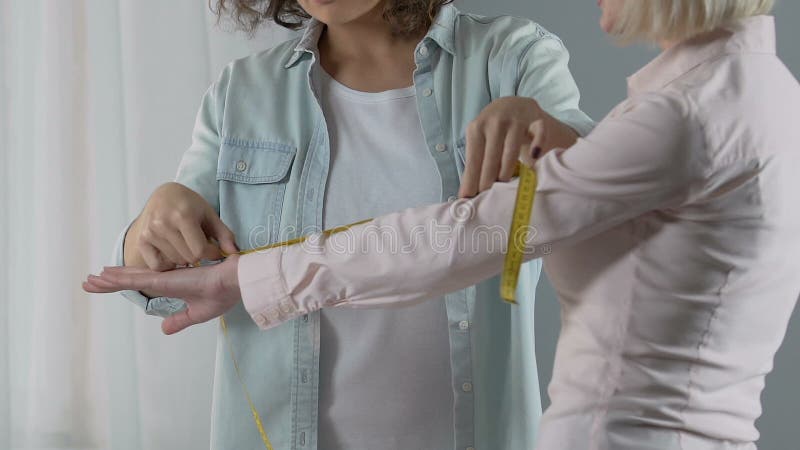 Progettista sorridente che misura il braccio femminile del cliente, discutente l'ordine del vestito