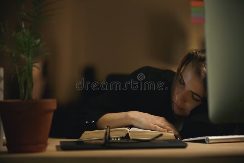 Progettista stanco della giovane signora che dorme all'interno alla notte sul libro fotografia stock libera da diritti Progettista stanco della giovane signora che dorme all'interno alla notte sul libro fotografia stock libera da diritti