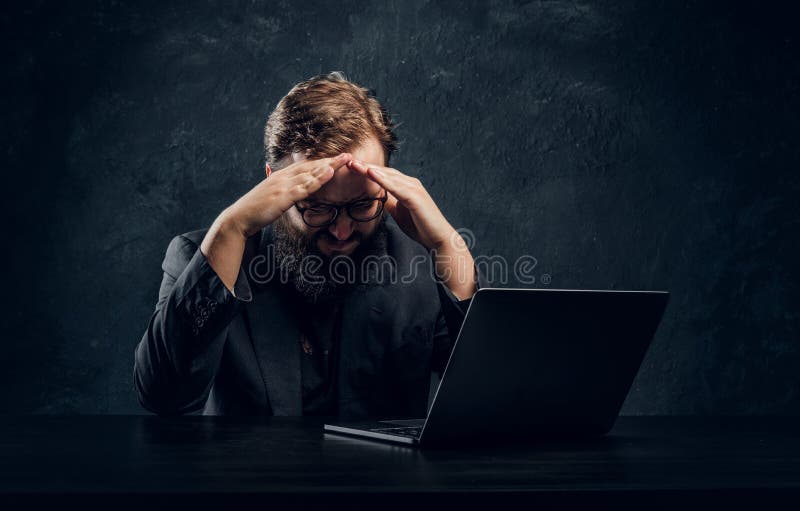 Programador barbudo cansado que se sienta en la tabla con el ordenador portátil en oficina imagen de archivo Programador barbudo cansado que se sienta en la tabla con el ordenador portátil en oficina imagen de archivo
