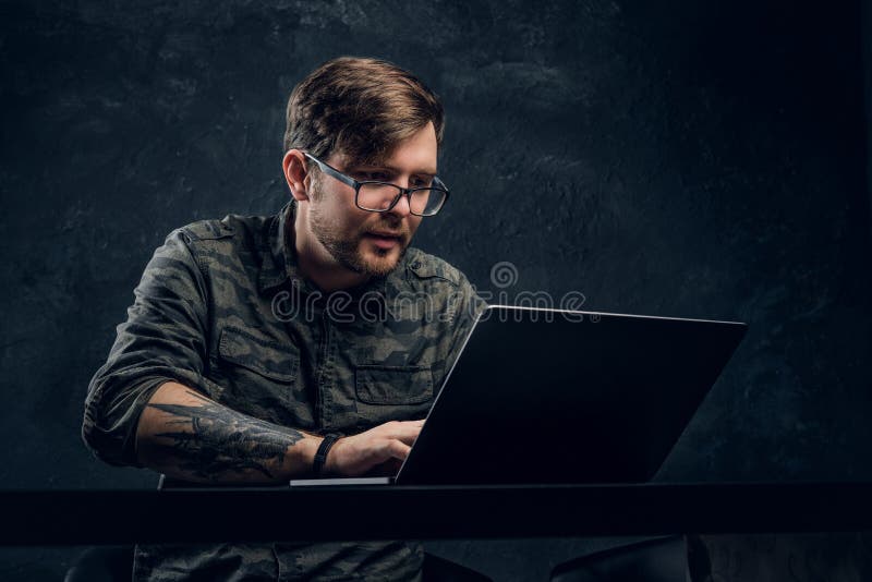 Programador que lleva un funcionamiento militar de moda de la camisa en el ordenador portátil que se sienta en la tabla en oficin fotos de archivo Programador que lleva un funcionamiento militar de moda de la camisa en el ordenador portátil que se sienta en la tabla en oficin fotos de archivo