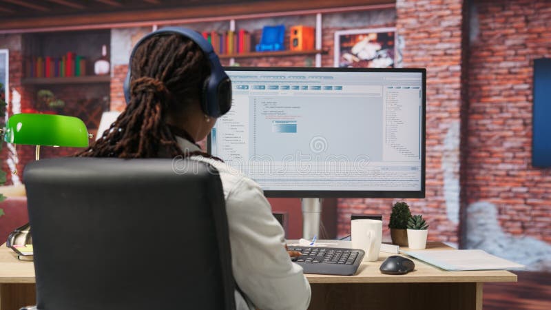 Programmer wearing headphones types code into PC, developing software programs, entering commands. Woman at home fixing errors in application, implementing new features, listening music, camera B. Developing programmer stock images, royalty-free photos and pictures