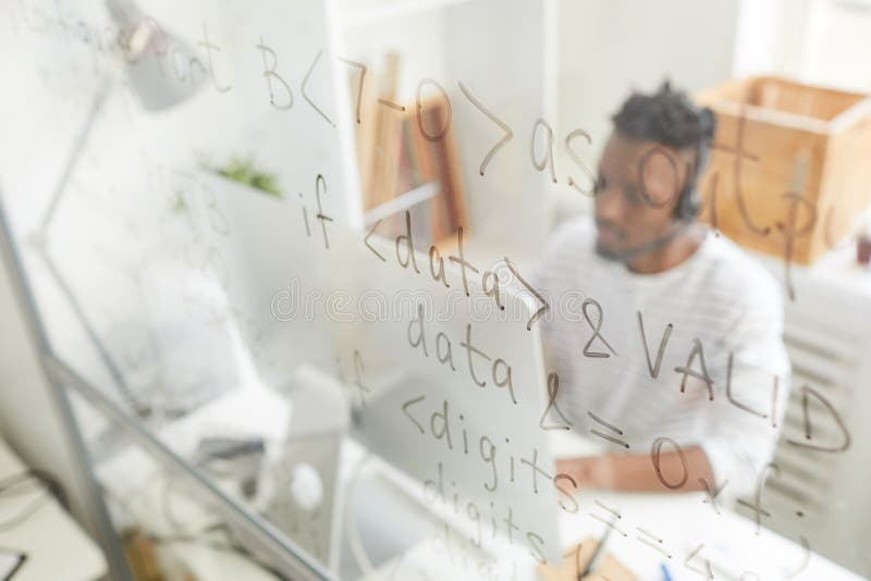 Programming code written on glassy board, African IT support operator in headset answering call and using computer in background. Source code script stock images, royalty-free photos and pictures