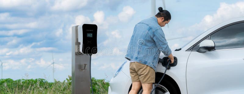 Progressive man with his EV car and wind turbine as concept of renewable energy.