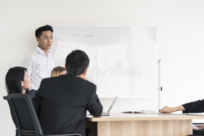 Projeto atual da placa do homem de negócios asiático novo aos colegas diversos interessados em negociações do escritório imagens de stock Projeto atual da placa do homem de negócios asiático novo aos colegas diversos interessados em negociações do escritório imagens de stock