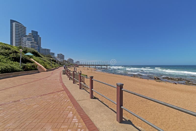 Promenade beach rocks ocean waves blue coastal city skyline. Paved Promenade beach sand rocks and ocean waves against blue coastal city skyline in Umhlanga stock image Promenade beach rocks ocean waves blue coastal city skyline. Paved Promenade beach sand rocks and ocean waves against blue coastal city skyline in Umhlanga stock image