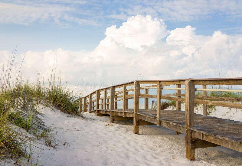 Inviting boardwalk through the sand dunes on a beautiful beach in the early morning. Beautiful puffy clouds in the sky. Inviting boardwalk through the sand dunes on a beautiful beach in the early morning. Beautiful puffy clouds in the sky.