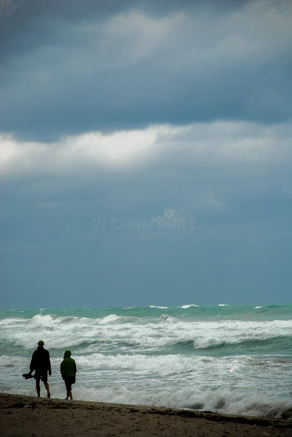 Promenade de deux personnes sur la plage par le mauvais temps photo stock Promenade de deux personnes sur la plage par le mauvais temps photo stock