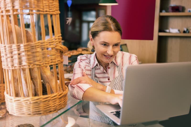 Contacting suppliers. Prosperous owner of bakery using her laptop while contacting suppliers making order. Contacting suppliers. Prosperous owner of bakery using her laptop while contacting suppliers making order