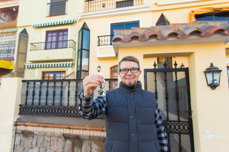 Propriété, propriété, nouvelle maison et concept de personnes - jeune homme avec des clés se tenant en dehors de la nouvelle mais images stock Propriété, propriété, nouvelle maison et concept de personnes - jeune homme avec des clés se tenant en dehors de la nouvelle mais images stock