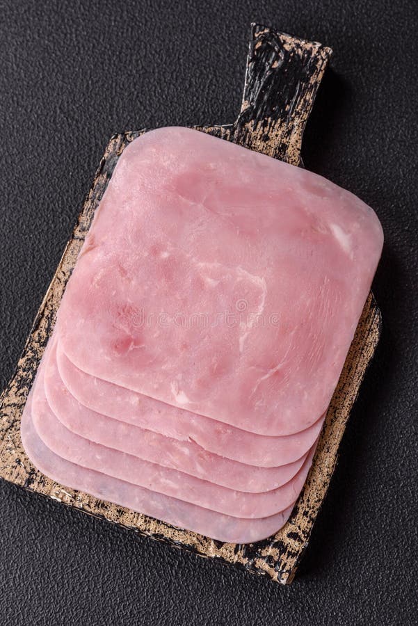 Prosciutto bollito tagliato a fette quadrate con acetosella e spezie. Prosciutto bollito tagliato a fette quadrate con acetosello e spezie su fondo di calcestruzzo scuro