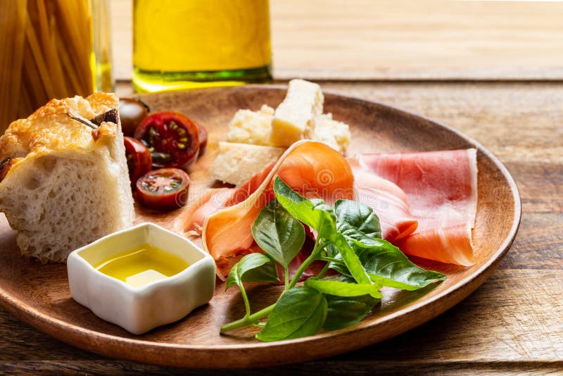 Italian ham, parmesan cheese, focaccia, tomato and basil twig in a wooden plate by a pasta jar and an olive oil bottle royalty free stock photography Italian ham, parmesan cheese, focaccia, tomato and basil twig in a wooden plate by a pasta jar and an olive oil bottle royalty free stock photography