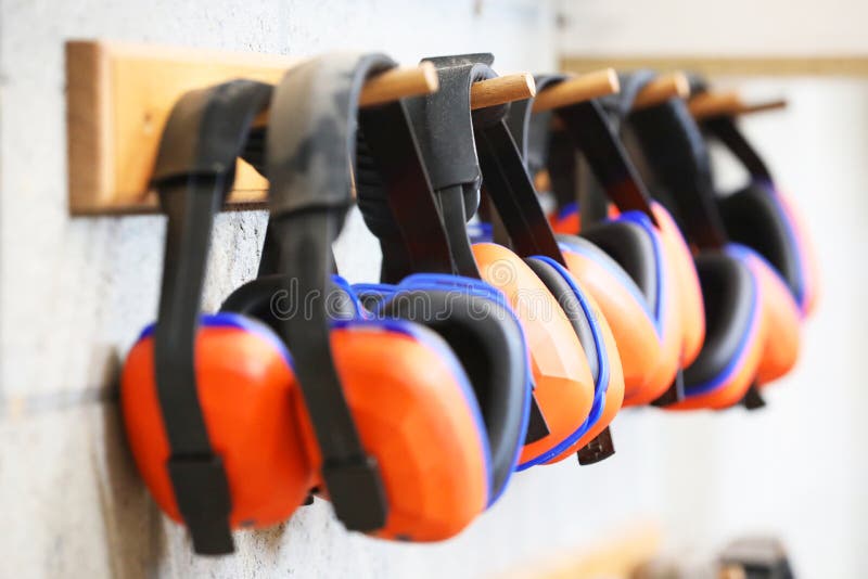 Row of orange ear muffs ear protection on a rack. workplace health and safety deafness concept. safe work practice. Row of orange ear muffs ear protection on a rack. workplace health and safety deafness concept. safe work practice