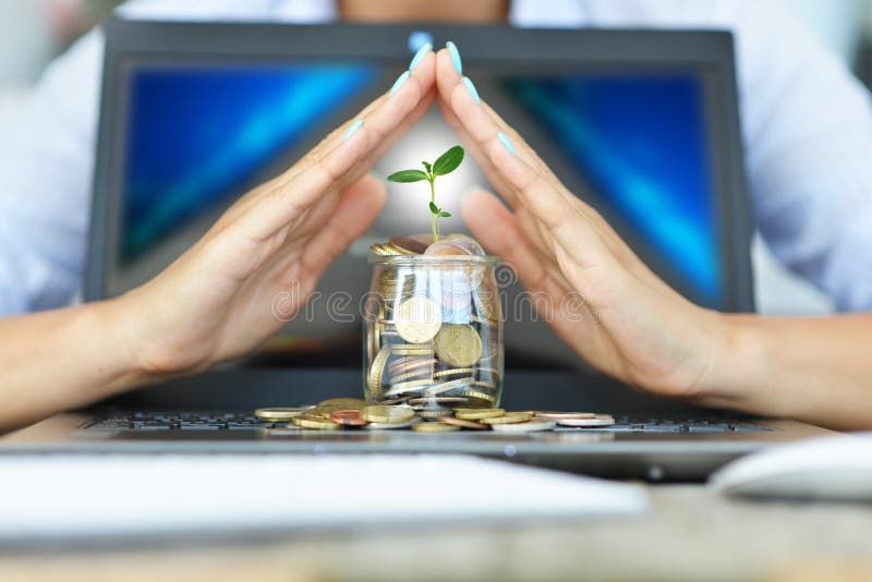 Protection of money from online transaction concept, with womanâ€™s hands covering a jar of coins above a notebook