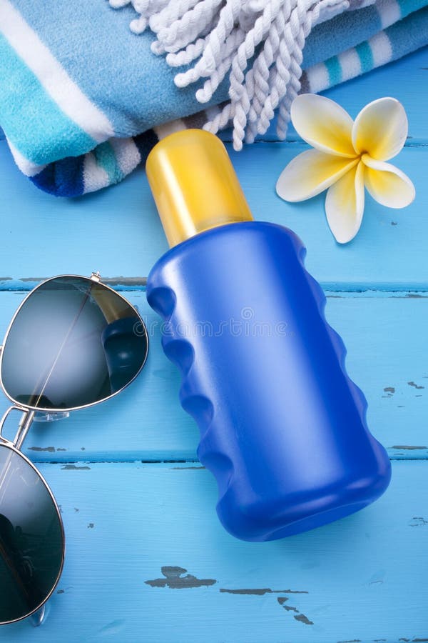 A bottle of sunscreen with a blank label, towel and sunglasses. A bottle of sunscreen with a blank label, towel and sunglasses