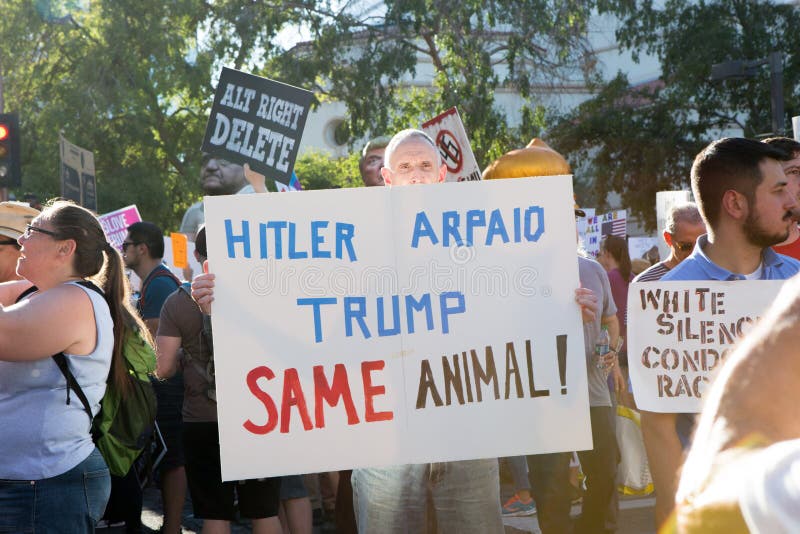 Phoenix, Arizona - August 22, 2017: Anti-Trump protester demonstrates outside of the Phoenix Convention Center while Trump delivers a speech, holding a Hitler, Arpaio and Trump are the same sign. Phoenix, Arizona - August 22, 2017: Anti-Trump protester demonstrates outside of the Phoenix Convention Center while Trump delivers a speech, holding a Hitler, Arpaio and Trump are the same sign