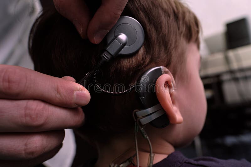 Hearing aid in the ear of a boy of 6-7 years old at a doctor`s appointment. Auditory testing and selection of treatment methods using auditing equipment. Faces are unrecognizable. Hearing aid in the ear of a boy of 6-7 years old at a doctor`s appointment. Auditory testing and selection of treatment methods using auditing equipment. Faces are unrecognizable
