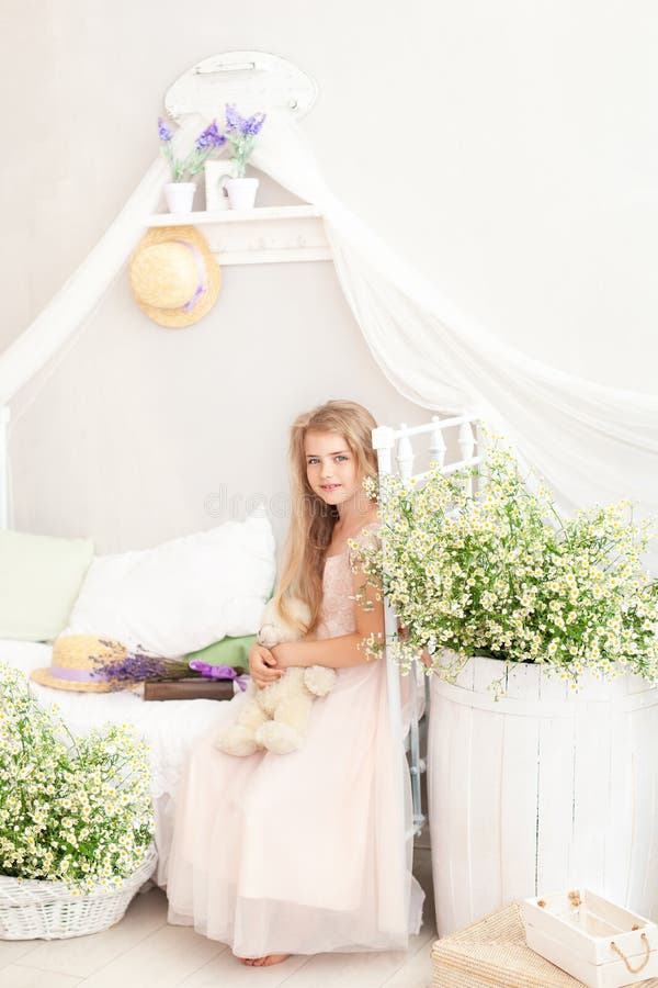Provence Porträtt av en liten flicka på sängen i ett ljust sovrum på morgonen Blonde söt flicka med långa hår kramar en teddy arkivfoton