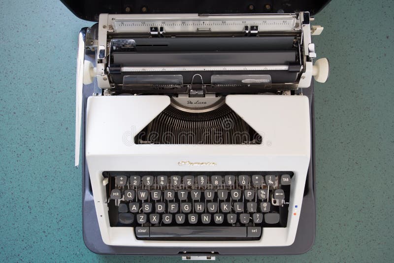 Portable metal typewriter, circa 1970, on a green desk in its open carrying case. May be used to symbolize journalism or creativity or an antiquated notion of portability. Either side may be used for copy space. Portable metal typewriter, circa 1970, on a green desk in its open carrying case. May be used to symbolize journalism or creativity or an antiquated notion of portability. Either side may be used for copy space.
