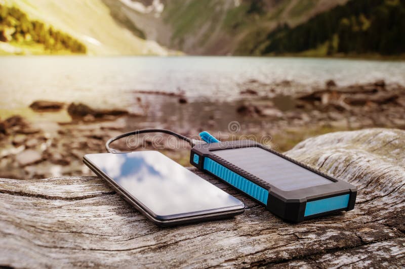 Portable solar panel for charging mobile devices lying on a log in the mountains where there is no electricity. Portable solar panel for charging mobile devices lying on a log in the mountains where there is no electricity