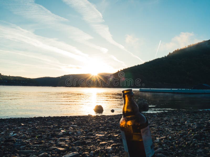 Przerzedże butelkę piwna pozycja na plaży przy wschód słońca obraz stock