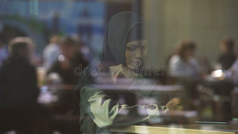 Przygnębiona kobieta w tradycyjnym Muzułmańskim hijab w kawiarni, trudności w nowym kraju