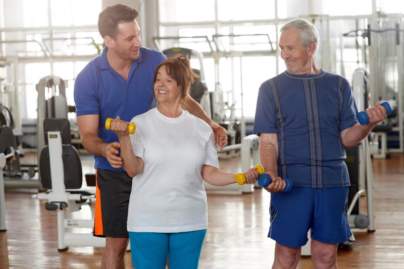 Przystojnego męskiego trenera instruowania starsza kobieta w gym zdjęcie stock Przystojnego męskiego trenera instruowania starsza kobieta w gym zdjęcie stock