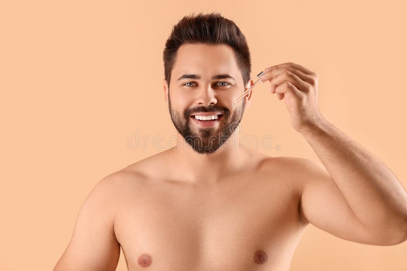 Przystojniak przyklejający surowicę kosmetyczną na beżowym tle zdjęcia royalty free