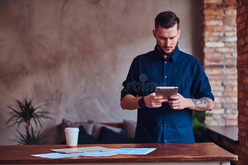 Handsome bearded man working with tablet in the office with loft interior. Handsome bearded man working with tablet in the office with loft interior.