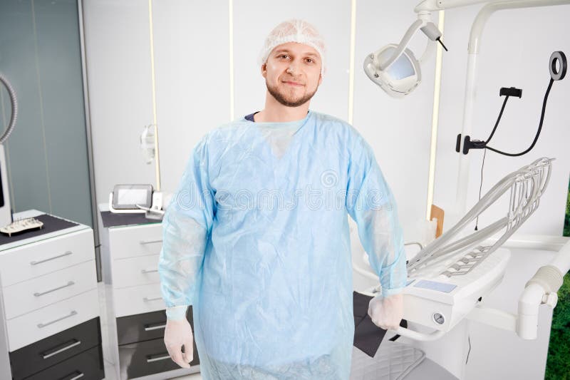 Przystojny dentysta w gabinecie dentystycznym. Widok z przodu młodego mężczyzny stomatologista patrzącego na kamerę i uśmiechającego się stojącego w nowoczesnym gabinecie dentystycznym. koncepcja stomatologii stomatologicznej i personelu stomatologicznego.