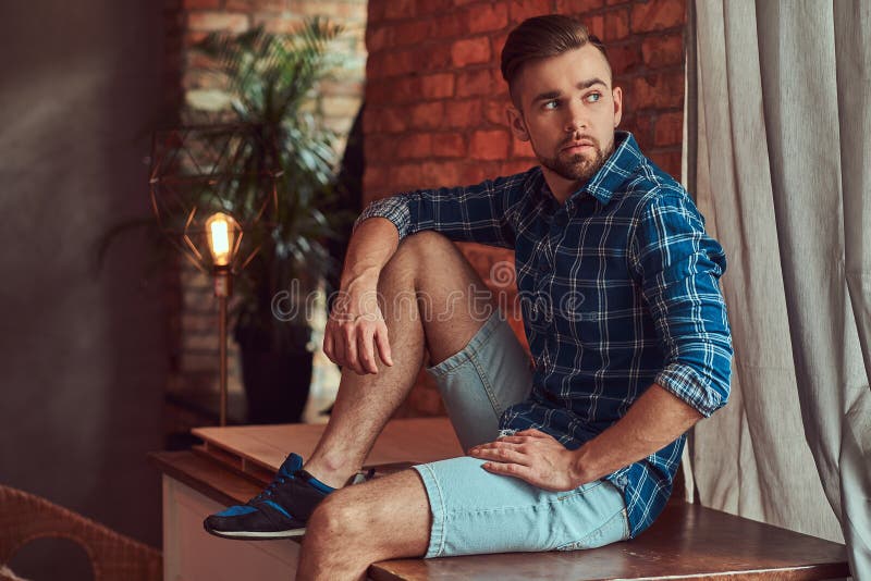 Handsome stylish hipster sitting on a table in a room with a loft interior. Handsome stylish hipster sitting on a table in a room with a loft interior.