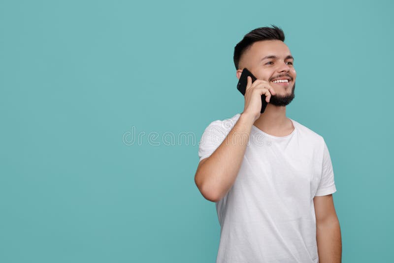Przystojny m?ody brodaty modni? w bia?ej koszulce u?ywa? telefon i opowiadaj?cy z jaskrawym u?miechem kosmos kopii fotografia royalty free Przystojny m?ody brodaty modni? w bia?ej koszulce u?ywa? telefon i opowiadaj?cy z jaskrawym u?miechem kosmos kopii fotografia royalty free