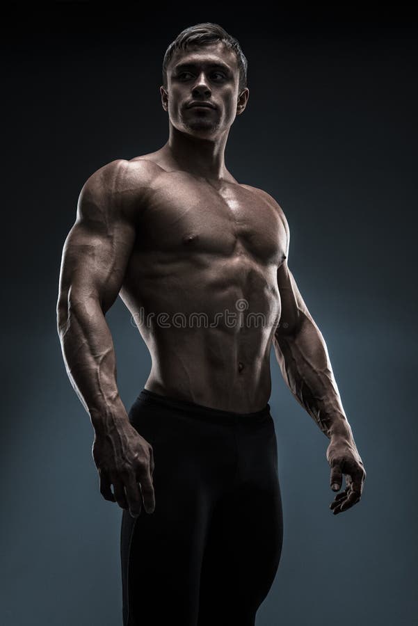 Przystojny mięśniowy bodybuilder pozuje nad czarnym tłem