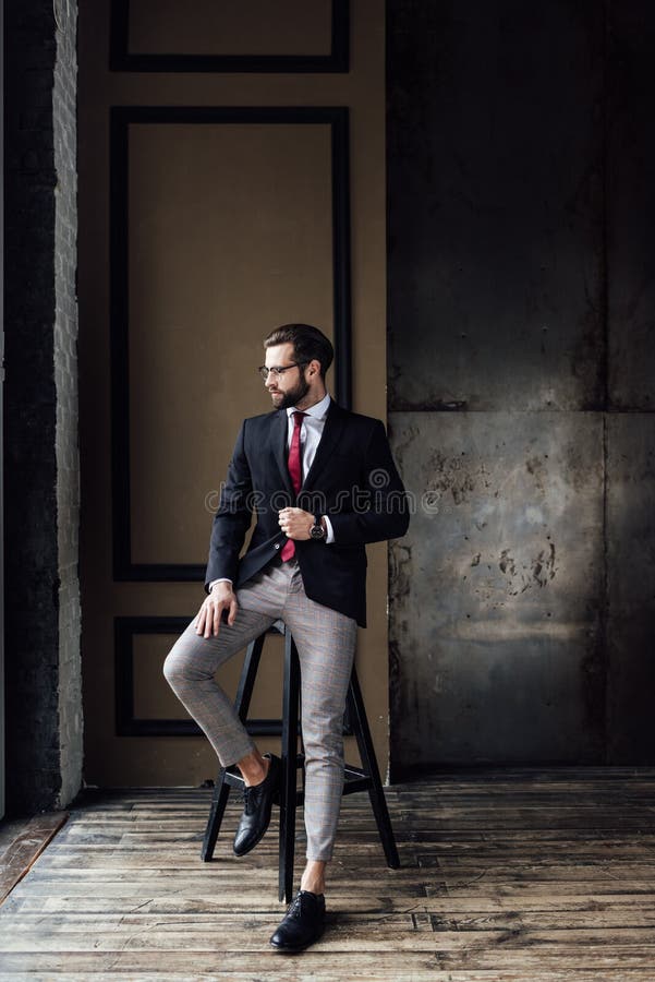 handsome fashionable businessman in suit posing on stool in loft interior. handsome fashionable businessman in suit posing on stool in loft interior