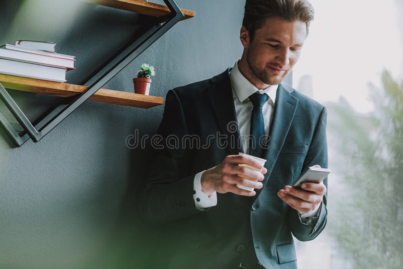 Przystojny mężczyzna patrzeje jego smartphone w kostiumu podczas gdy stojący obrazy stock Przystojny mężczyzna patrzeje jego smartphone w kostiumu podczas gdy stojący obrazy stock