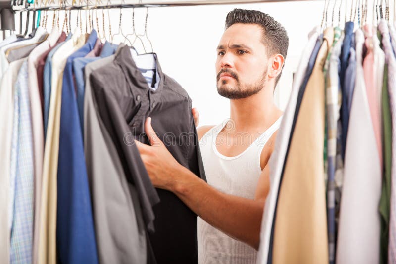 Portrait of an attractive young man with a beard trying to find the right shirt to wear today on his closet. Portrait of an attractive young man with a beard trying to find the right shirt to wear today on his closet
