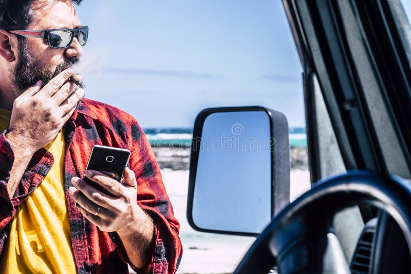 Przystojny mężczyzna stojący z cygarem korzysta z telefonu komórkowego poza czarnym samochodem - plaża i ocean w tle do podróży i obraz stock Przystojny mężczyzna stojący z cygarem korzysta z telefonu komórkowego poza czarnym samochodem - plaża i ocean w tle do podróży i obraz stock
