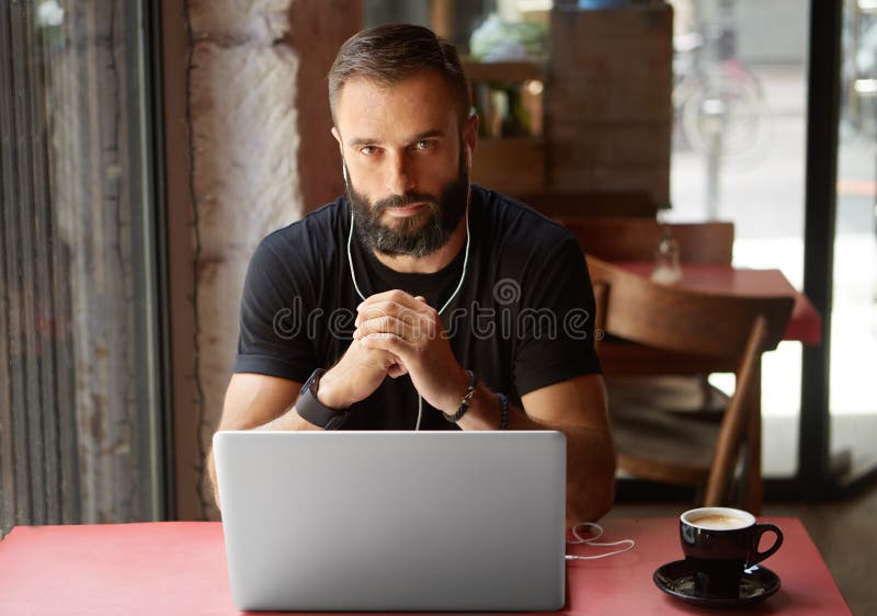 Przystojny Młody Brodaty biznesmen Jest ubranym Czarnego Tshirt Pracującego laptopu Miastowej kawiarni Mężczyzna drewna stołu fil obraz stock Przystojny Młody Brodaty biznesmen Jest ubranym Czarnego Tshirt Pracującego laptopu Miastowej kawiarni Mężczyzna drewna stołu fil obraz stock