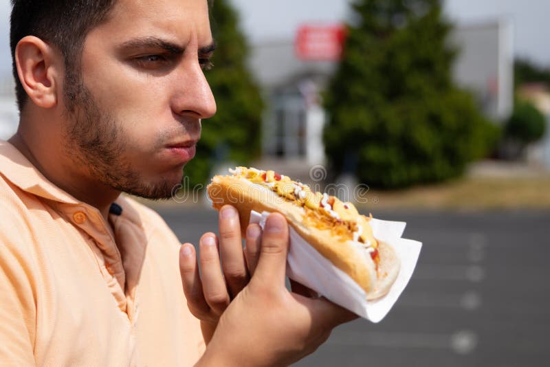 Przystojny młody brunetka mężczyzny łasowania hot dog obraz royalty free Przystojny młody brunetka mężczyzny łasowania hot dog obraz royalty free