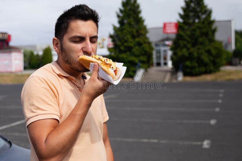 Przystojny młody brunetka mężczyzny łasowania hot dog zdjęcie stock Przystojny młody brunetka mężczyzny łasowania hot dog zdjęcie stock