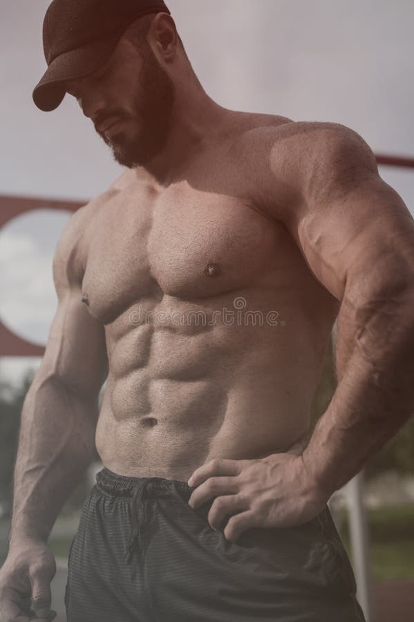 Przystojny, silny młody człowiek z brodą w czarnej czapce z doskonałymi mięśniami brzucha stojący na zewnątrz trening siłowni
