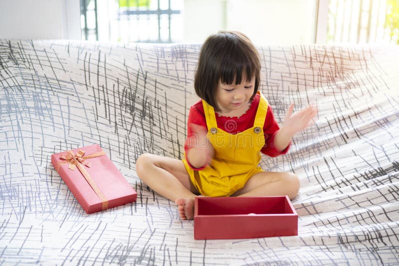 Präsentieren eine überrascht jung asiatisch mädchen sitzt auf einem sofa öffnen ein geschenk lizenzfreie stockbilder