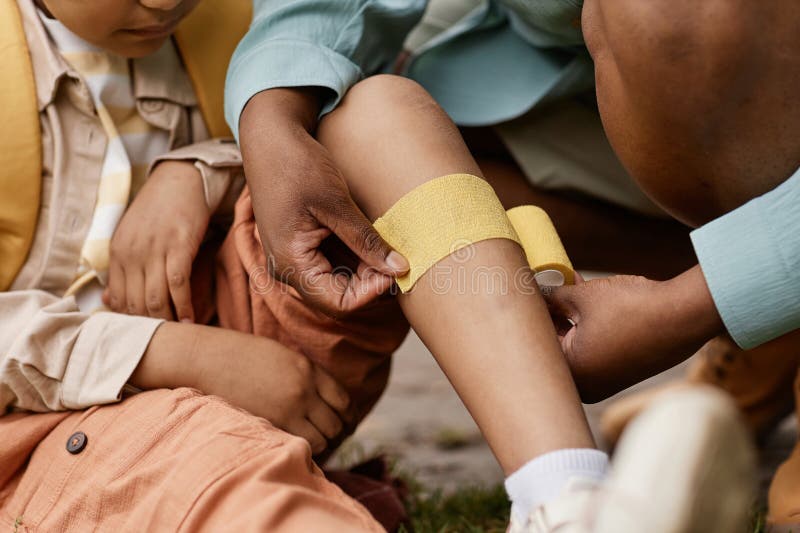 Près d'une mère mettant des bandages sur les enfants genoux à l'extérieur photo libre de droits